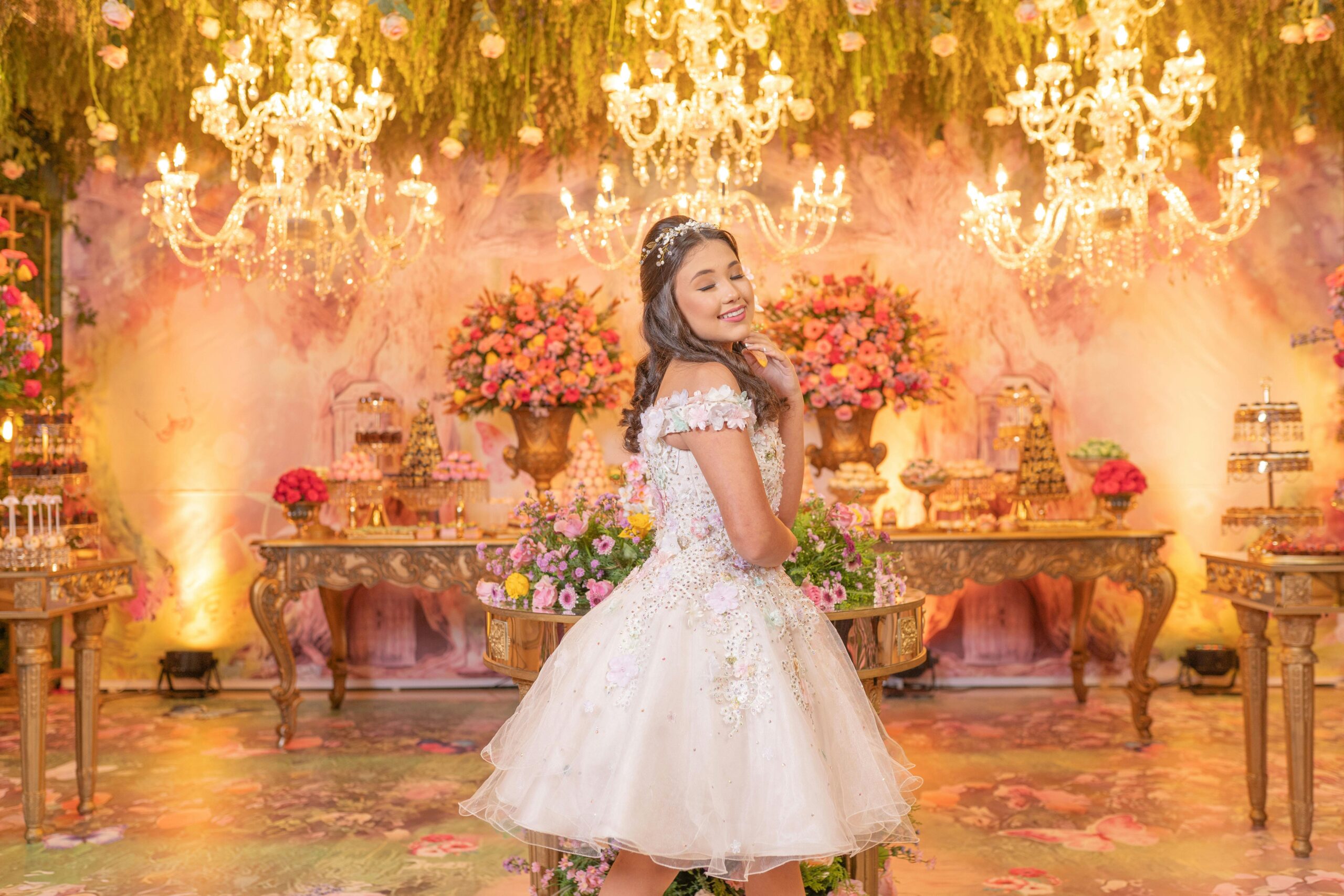 Teen girl celebrating quinceañera in a luxurious, floral decorated room with chandeliers.
